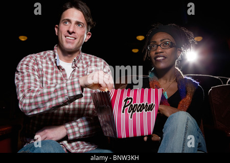 Couple eating popcorn in movie theatre Stock Photo