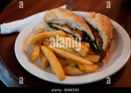 A fried chicken sandwich on ciabatta bread served with chips at a typical English pub in London. Stock Photo