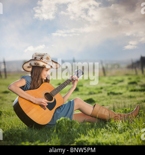 Cowgirl playing guitar in field Stock Photo