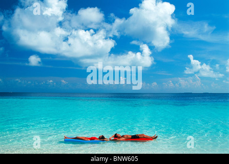 Couple floating in paradise under puffy white clouds on colorful air mattresses during idyllic island holiday Stock Photo