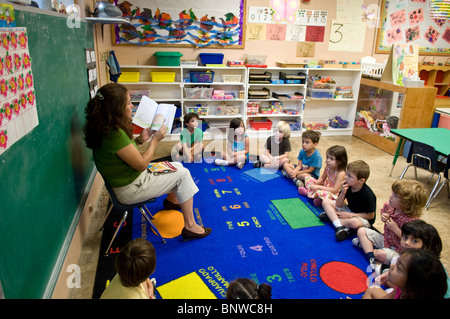 Hispanic female teacher reads book in Spanish to group of multi-ethnic pre-kindergarten age children at bilingual nursery school Stock Photo