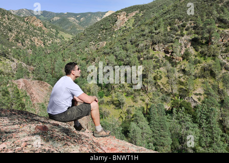 Handsome young man sitting on the rock enjoying the view. Stock Photo