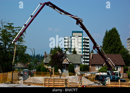 Concrete pumper truck uses extra long hydraulic arm hose pipe to reach foundation forms at house construction site Stock Photo