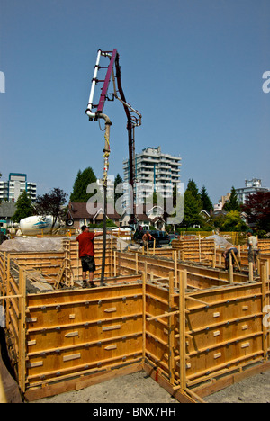 Concrete pumper truck uses extra long hydraulic boom pipe to reach plywood foundation forms at Vancouver house construction site Stock Photo