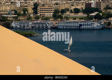feluccas and cruise ships sailing in front of a sand dune on the Nile River in Aswan Egypt Stock Photo