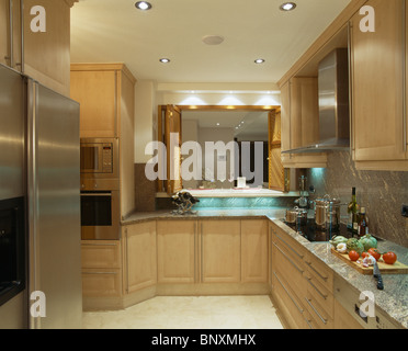 Recessed lighting in modern in modern Spanish kitchen with pale wood fitted units and large American-style fridge-freezer Stock Photo