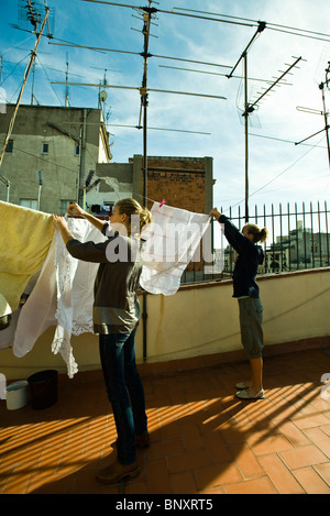 Sisters hanging laundry to dry on rooftop clothes-line Stock Photo
