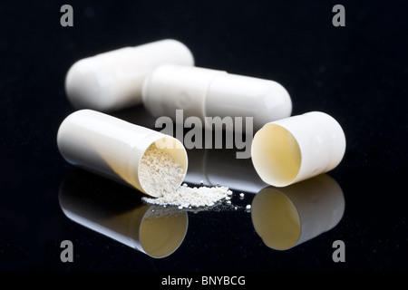 close-up of three white medical capsules , (one  opened), isolated on black background Stock Photo