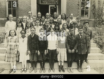 Circa 1900 school photo, showing a group of caucasian 9-11 years old with an African American girl. Stock Photo
