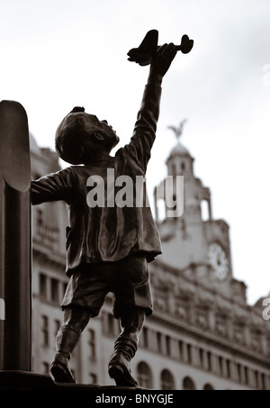 Statue of a boy with a toy plane in the Our lady and St Nicholas Church garden.  In the background is the Liver Building.  The statue comemerates Liverpudleans who died in the blitz.  Sculptor: Tom Murphy Stock Photo