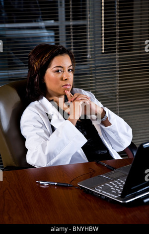 African-American woman in lab coat thinking at desk Stock Photo