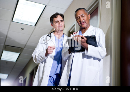 Mature doctors conversing, reviewing chart, in office corridor Stock Photo