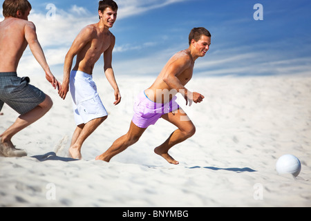 Young men playing soccer on beach.