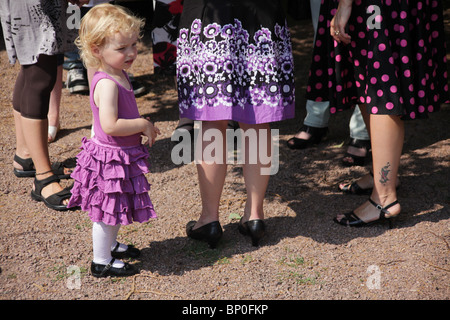 Little girl toddler in party clothes dressed up standing among women mother aunty legs MODEL RELEASED Stock Photo