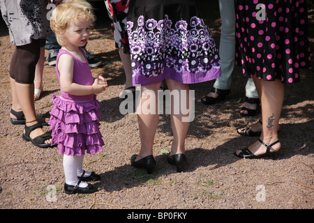 Little girl toddler in party clothes dressed up standing among women mother aunty legs MODEL RELEASED Stock Photo