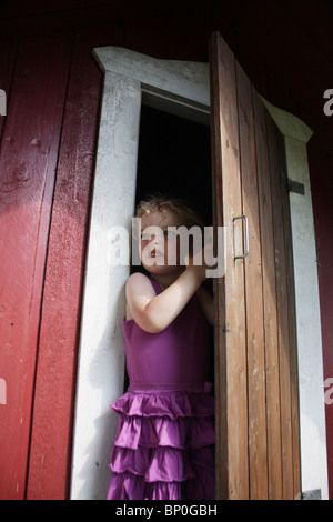 Little girl toddler in party clothes opening an outside wooden playhouse door MODEL RELEASED Stock Photo