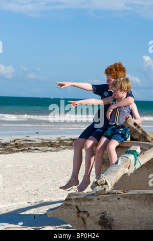 Kenya, Coast, Diani Beach. Two boys sit on a dug-out canoe whle on holiday on Galu Beach. (MR) Stock Photo