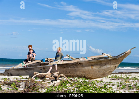 Kenya, Coast, Diani Beach. Three boys sit on a dug-out canoe whle on holiday on Galu Beach. (MR) Stock Photo