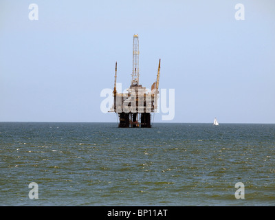 A sail boat passes a large offshore oil rig. Stock Photo