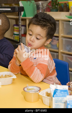 Preschool boy drinking juice and eating breakfast in the school classroom Stock Photo