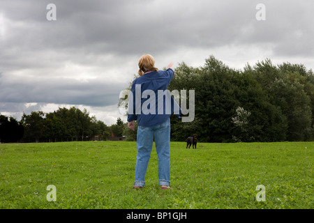 A lady uses a flinger to throw a tennis ball for her Labradoodle dog in a countryside park with a storm imminent Stock Photo