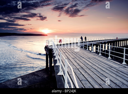 Whitby pier with the sun setting beyond Kettleness point. Stock Photo