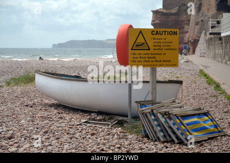 a boat and deck chairs tied up on the caution sign on sidmouths pebbly beach Stock Photo