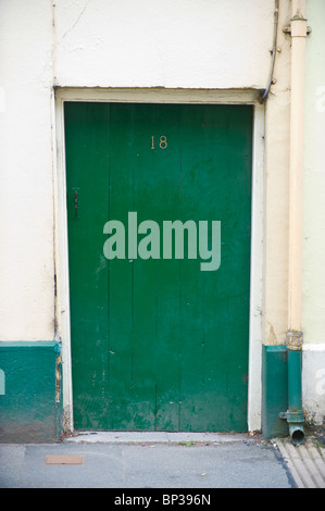 Rustic scruffy green painted wooden paneled front door no. 18 of cottage in UK Stock Photo