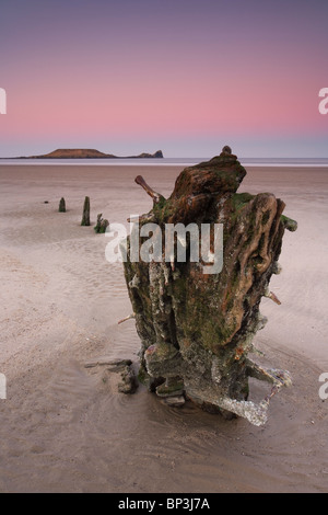 The partially buried wreck of The Helvetia with a view towards Worms Head at on Rhossili Beach Gower Peninsula South Wales UK Stock Photo