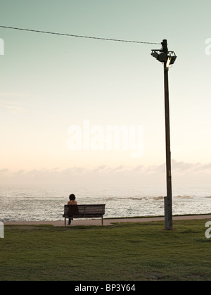 Woman sitting on Bench in park watching sunrise sunset over ocean Stock Photo