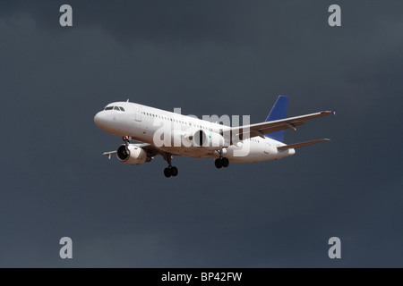 Airbus A320 passenger jet plane flying on approach in a dark cloudy sky. No livery and proprietary details deleted. Commercial air travel, aviation. Stock Photo