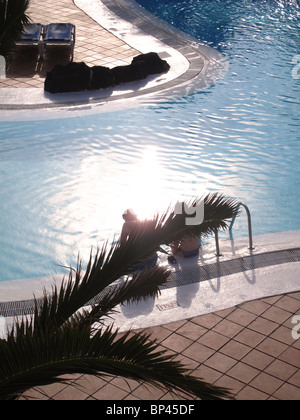 couple sitting at edge of apartment swimming pool Stock Photo