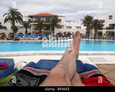 Mans feet on sunbed by pool Stock Photo