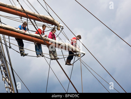 Members of the crew of a square rigged sailing ship working on the middle spar of one of the masts. Stock Photo