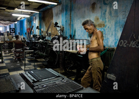 A Cuban master printer, leant against a printing machine, waiting for a new load in the print shop, Santiago de Cuba, Cuba. Stock Photo