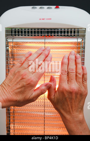 Everyday scene of one senior woman warming hands in front of a low energy Halogen room heater. England UK Britain Stock Photo