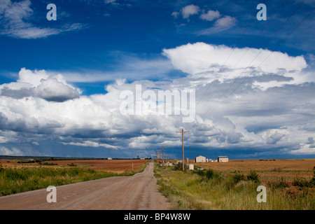 Picturesque scene of a farm along a dirt road in a vast rural landscape with cumulus cloud formations in southwest Colorado Stock Photo