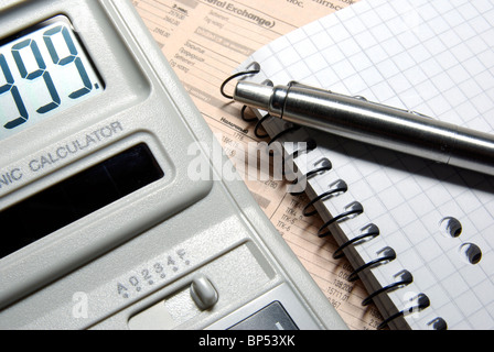 Calculator with numbers on display, pen and notebook laying on newspaper. Stock Photo