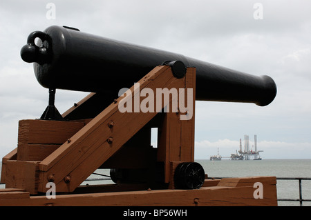 Civil War era cannon atop Fort Gaines rampart overlooks natural gas drilling rig at mouth of Mobile Bay Alabama Stock Photo