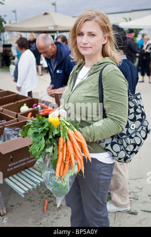 Woman holding fresh carrots at an outdoor farmers market, St. Norbert Farmers Market, Winnipeg, Manitoba, Canada. Stock Photo