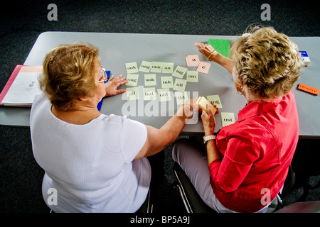 Using 'word card' components to form a complete word, a volunteer adult literacy teacher instructs an elderly Hispanic student. Stock Photo