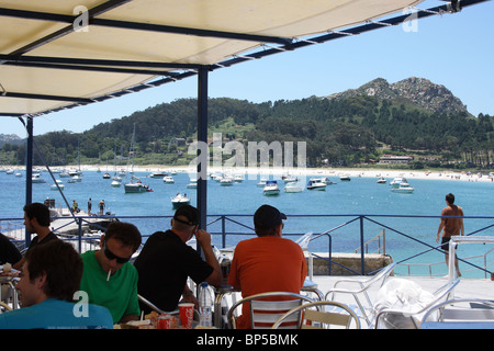 People at outdoor cafe tables of restaurant on beach, Isla de Monte Faro, Islas Cies, Vigo, Galicia, Spain, beach and boats Stock Photo