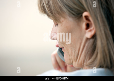 Close up of a middle aged woman talking on a telephone while seated outside in a residential yard. Stock Photo
