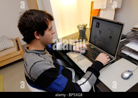 young man connected to Facebook using his laptop in his room in Austria Stock Photo
