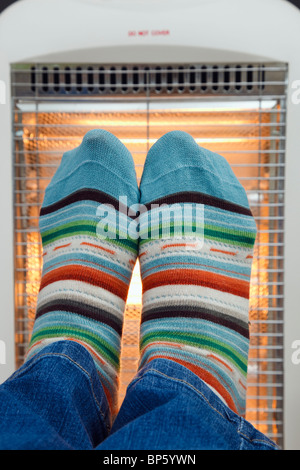Some person wearing colourful matching pair striped woolly socks warming feet in front of a low energy electric Halogen room heater.