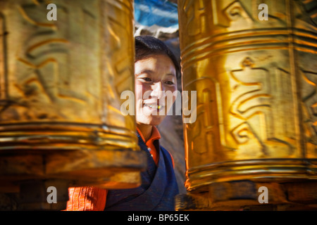 A female pilgrim spins golden mani prayer wheels on the Tashilhunpo kora in Shigatse, Tibet Stock Photo