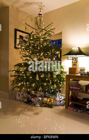 Vertical wide angle of a decorated real spruce Christmas tree with lots of presents underneath inside a modern minimalist home. Stock Photo