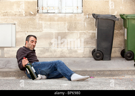poor drunk man lying near trashcan in city street Stock Photo