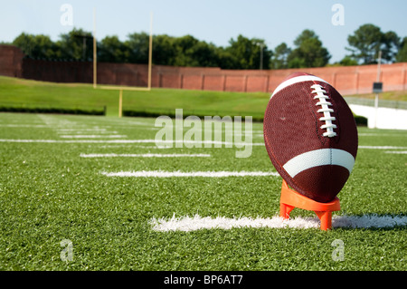 American football on kicking tee on field with goal post in background. Stock Photo