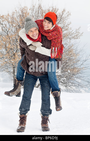 Young man giving his girlfriend piggyback in snow Stock Photo